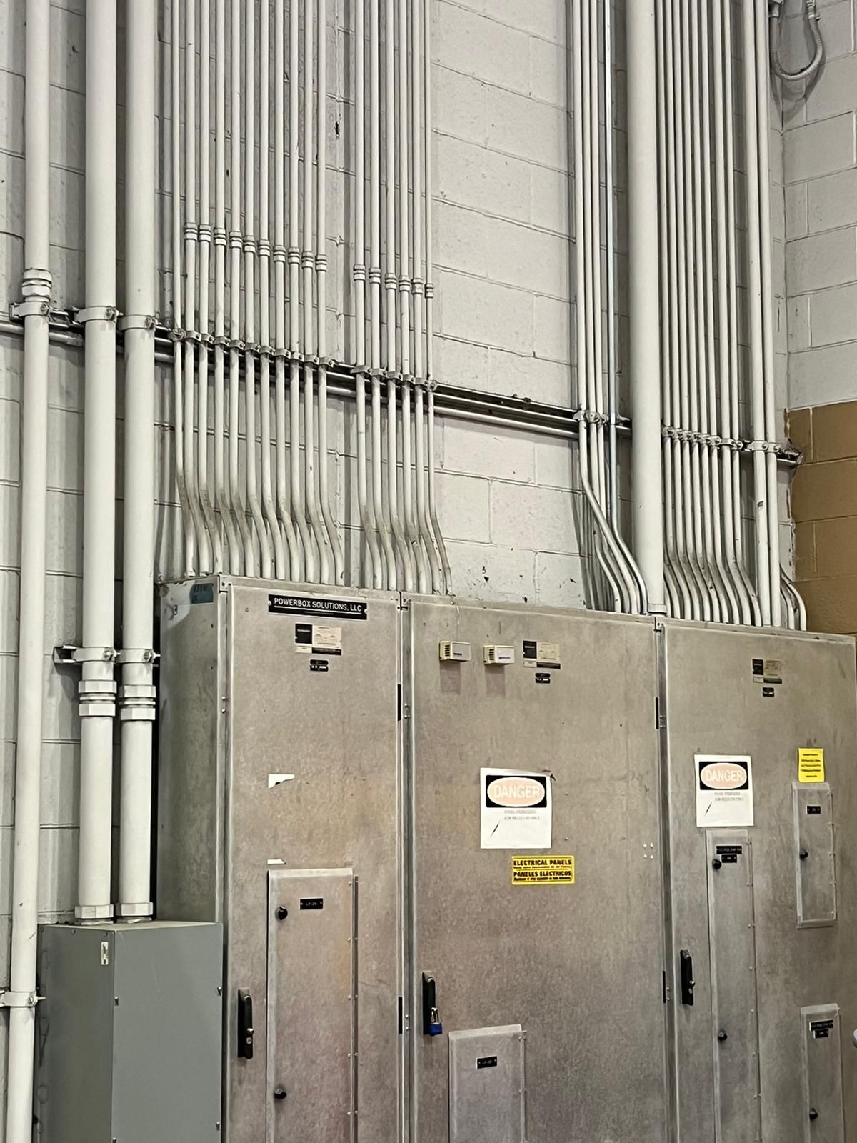 Electrical panel with conduit piping against a gray cinderblock wall.