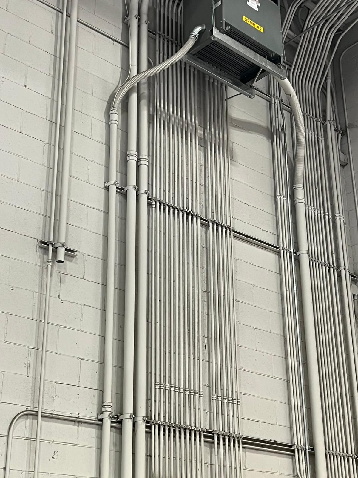 Electrical conduits mounted on a gray concrete wall, leading to a box-shaped device.
