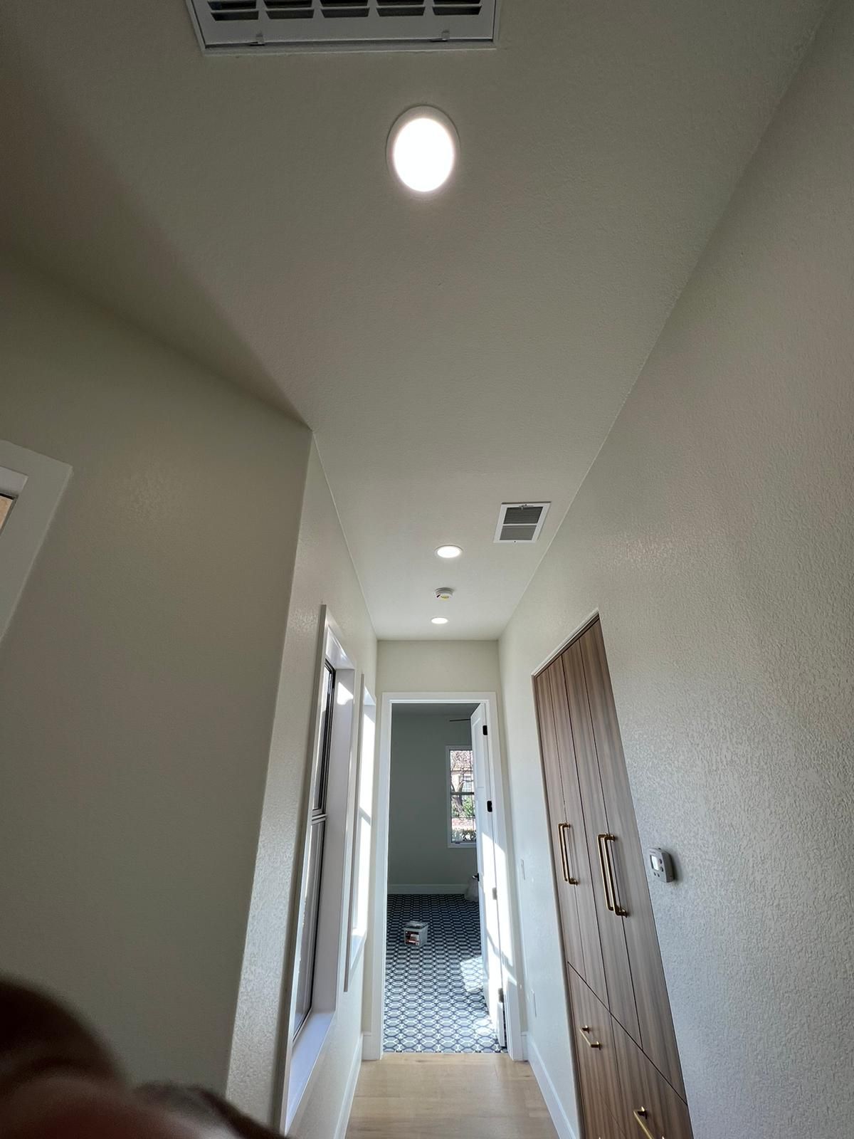 Hallway with recessed ceiling lights and a patterned tile floor at the end, leading to a door.