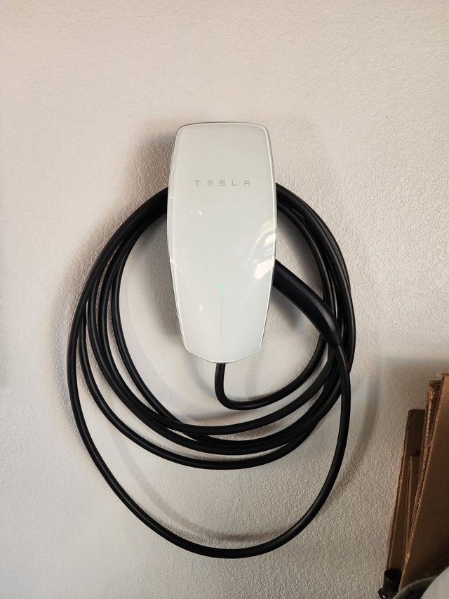 White Tesla charger mounted on a wall with coiled black charging cable.