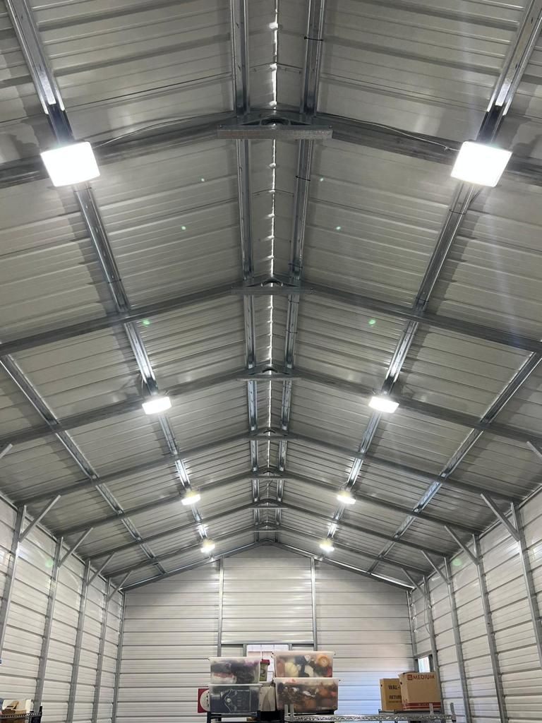 Interior of a metal building with overhead lighting fixtures. The roof is sloped with metal beams and panels.