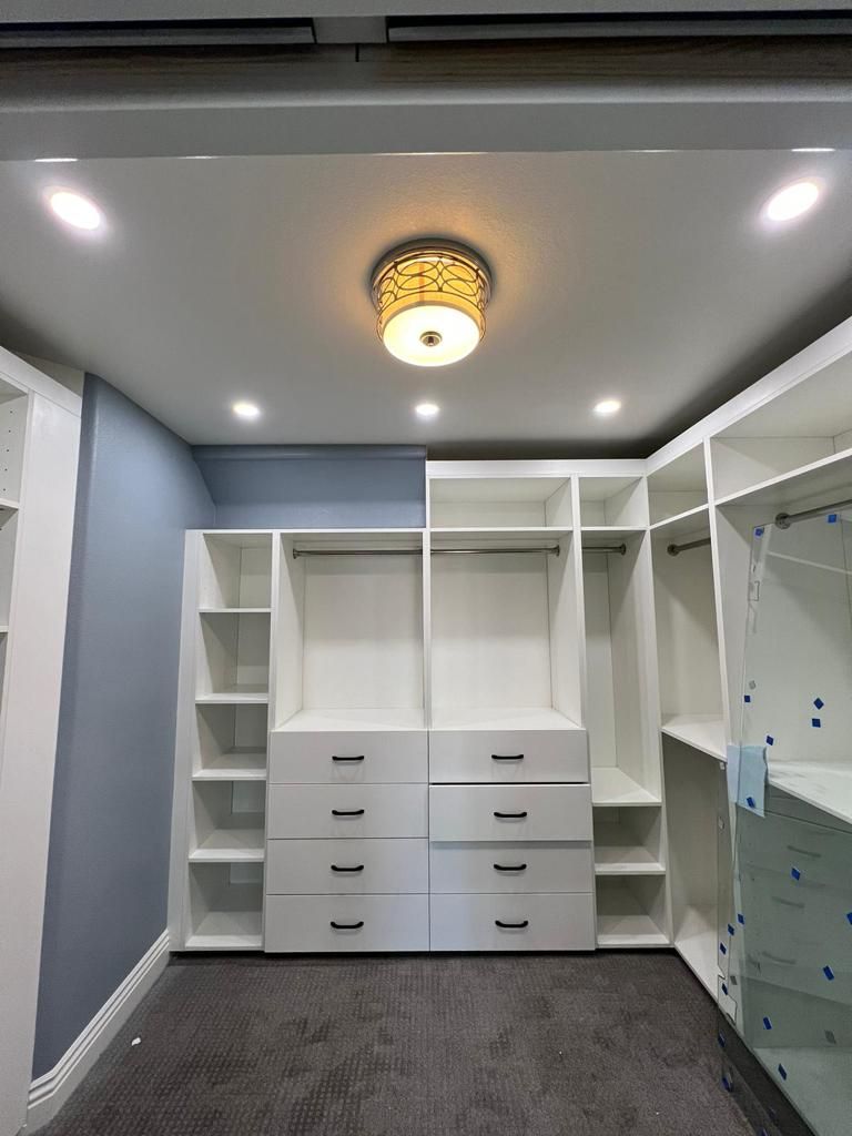 White walk-in closet with shelves, drawers, and hanging rods. Gray carpet, recessed lights, and a decorative ceiling light.