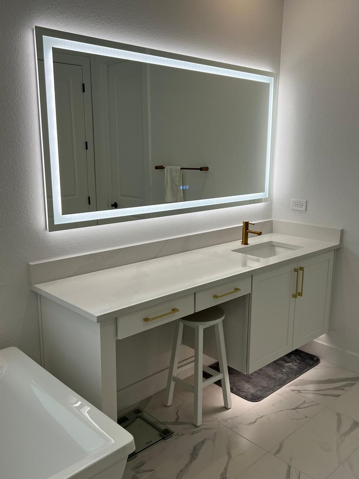 White bathroom vanity with lighted mirror, sink, and stool.