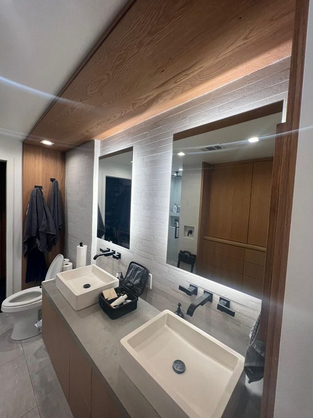 Bathroom with two sinks, two mirrors with lights, wood accents, and gray walls.