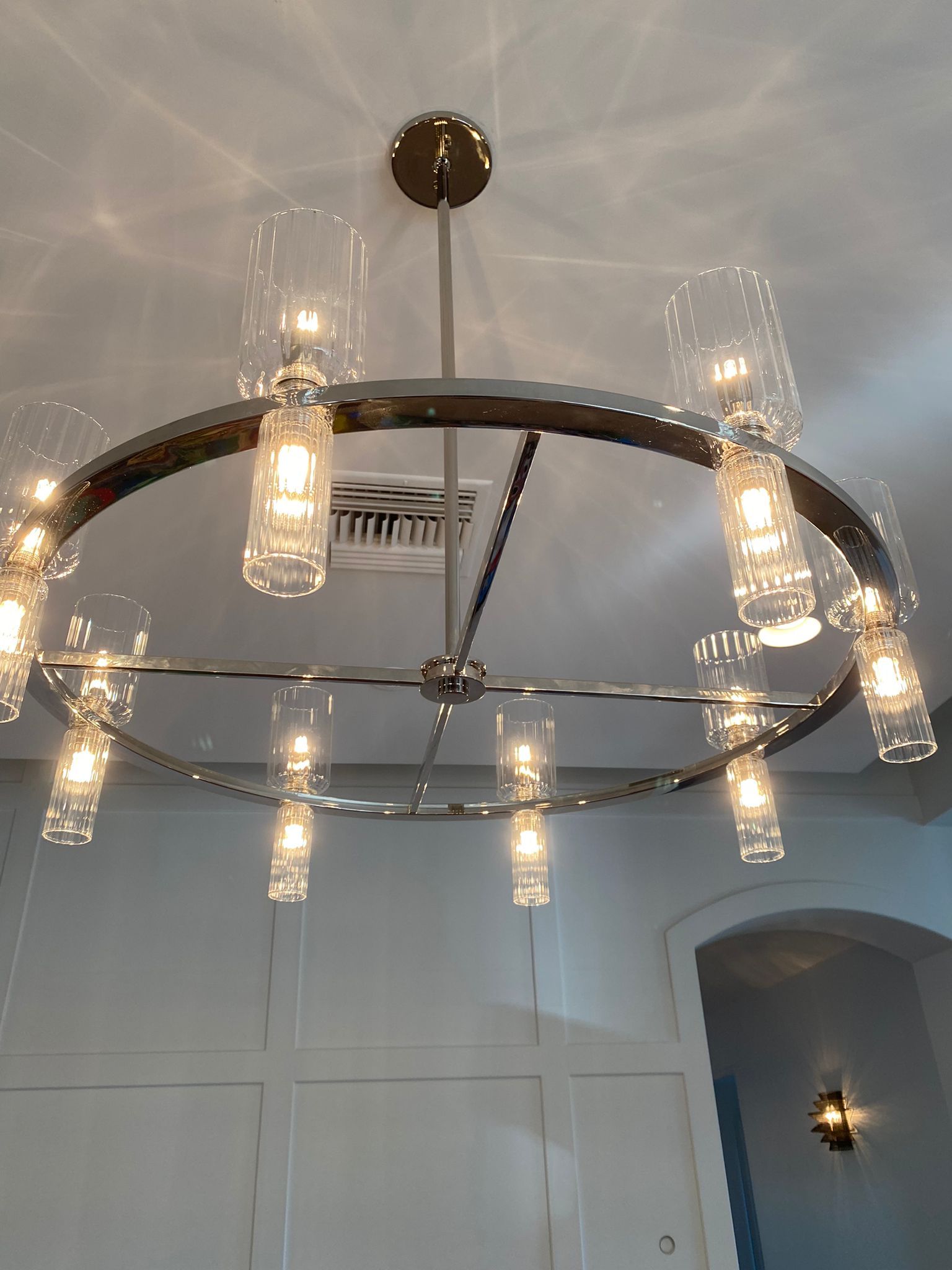Circular chandelier with clear glass shades, mounted on a white ceiling, above a white-paneled wall and doorway.