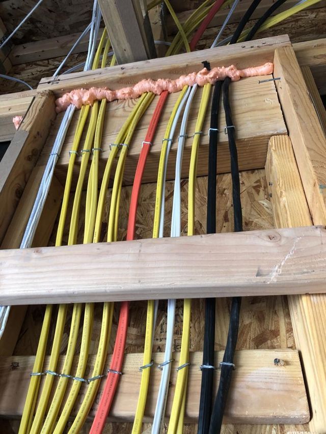 Electrical wiring, yellow, orange, and black cables, secured with metal clips, running through wooden frame.