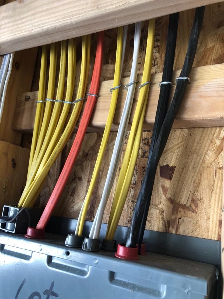Electrical wires of various colors entering a metal box, secured by clips, inside a wooden frame.