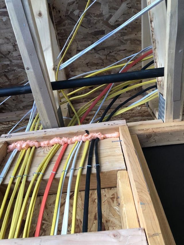 Electrical wiring and plumbing in a wooden ceiling framing. Yellow, black, white, and red wires are visible.