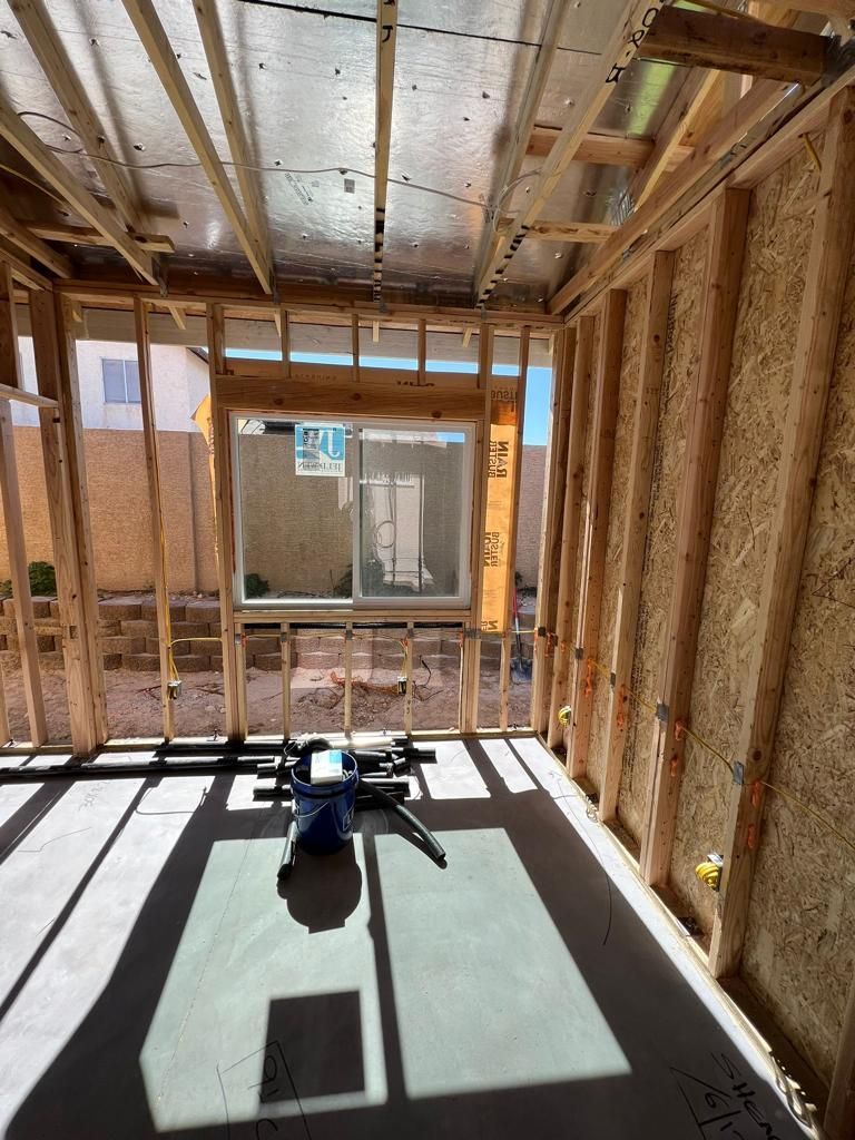 Interior of a room under construction with exposed wooden framing and a window overlooking a yard.