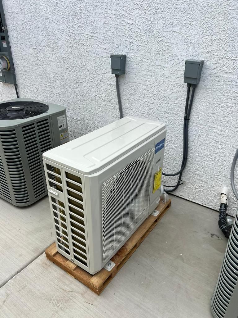Air conditioning units on a pallet next to a building. Power cords are attached.