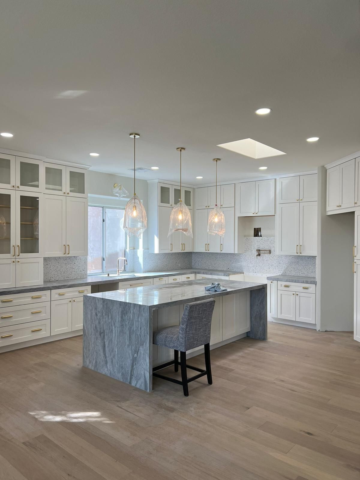 Spacious white kitchen with island, wood floors, and pendant lights.