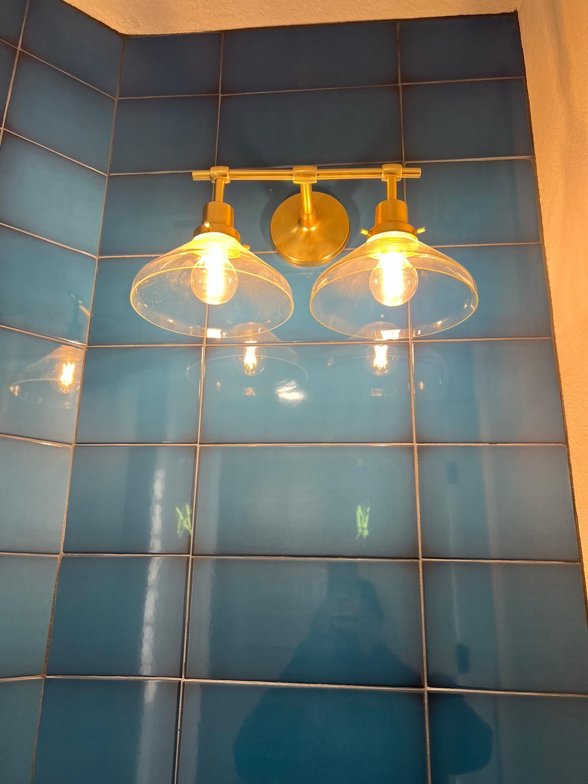 Brass vanity light fixture with two clear glass shades on blue tiled wall.
