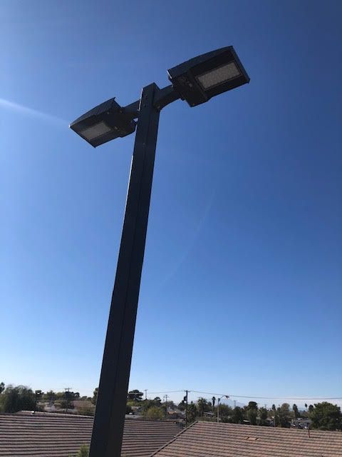 Tall, black light pole with two rectangular LED lights against a clear blue sky.