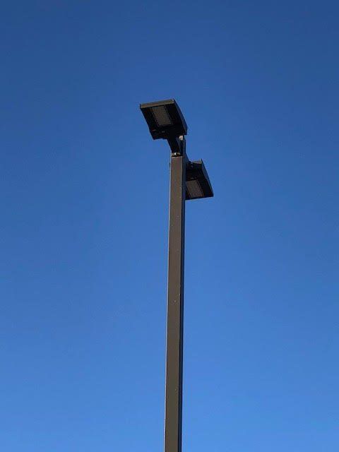 Dark gray street light against a clear, blue sky. Two rectangular LED lights are mounted atop the pole.