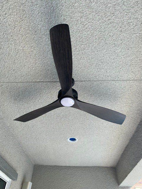 Ceiling fan with three dark blades and a central light fixture on a textured ceiling.