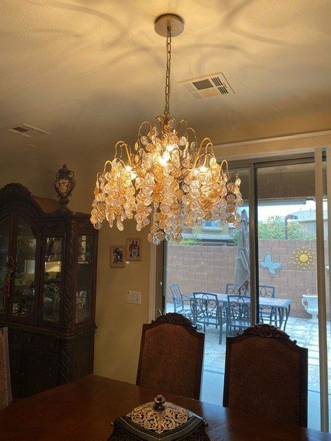 Crystal chandelier in a dining room, overlooking a patio with furniture through sliding glass doors.
