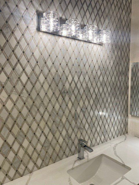 Bathroom with diamond-patterned tile wall, illuminated by a multi-light fixture, over a white countertop and sink.