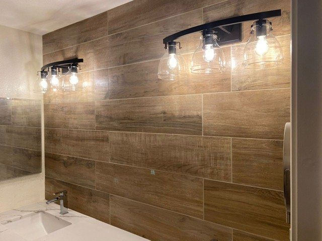 Bathroom with wood-look tile wall and two black light fixtures with clear glass shades. A white sink is below.