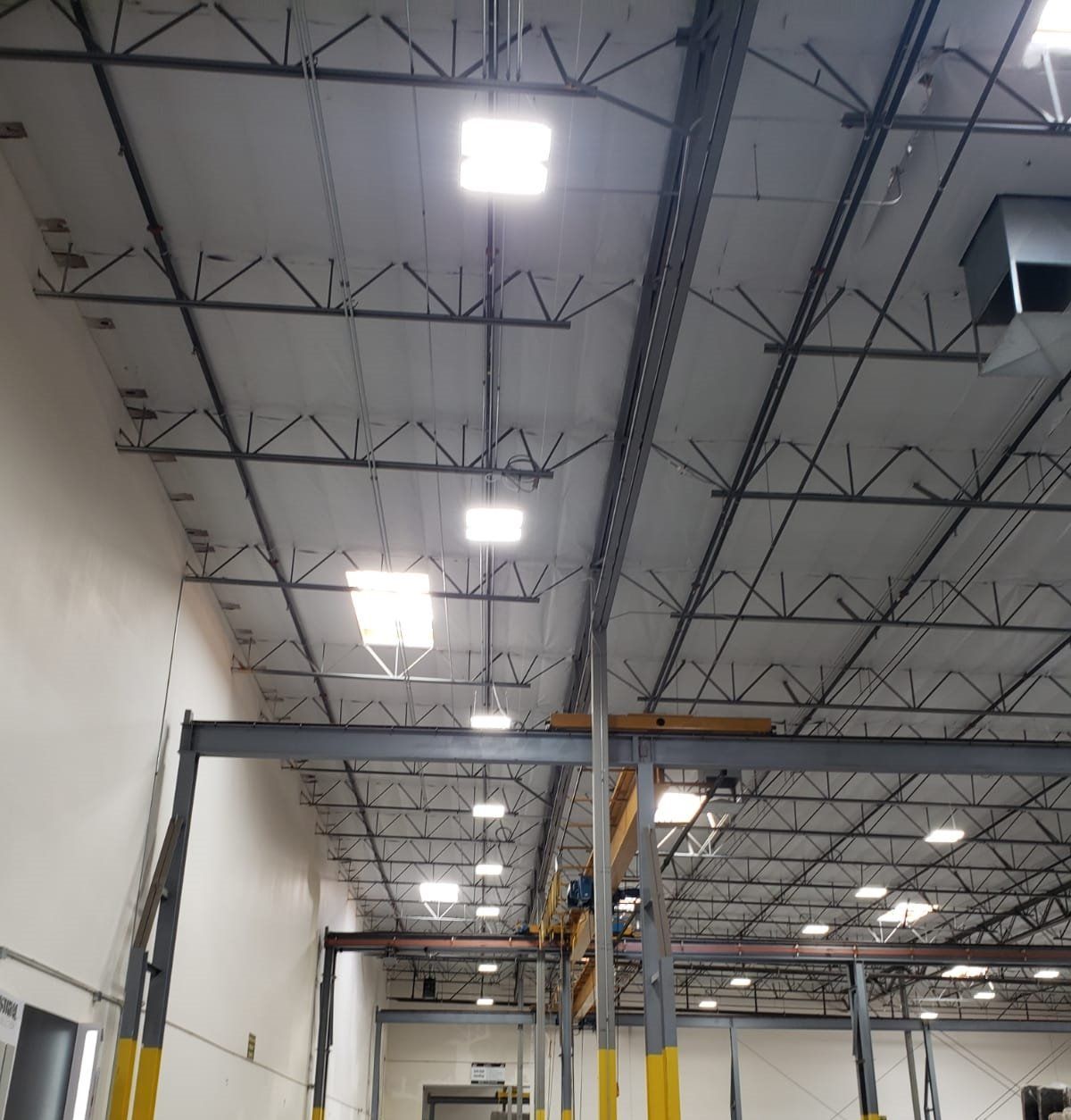 Warehouse interior with a high ceiling, metal beams, and overhead lights.