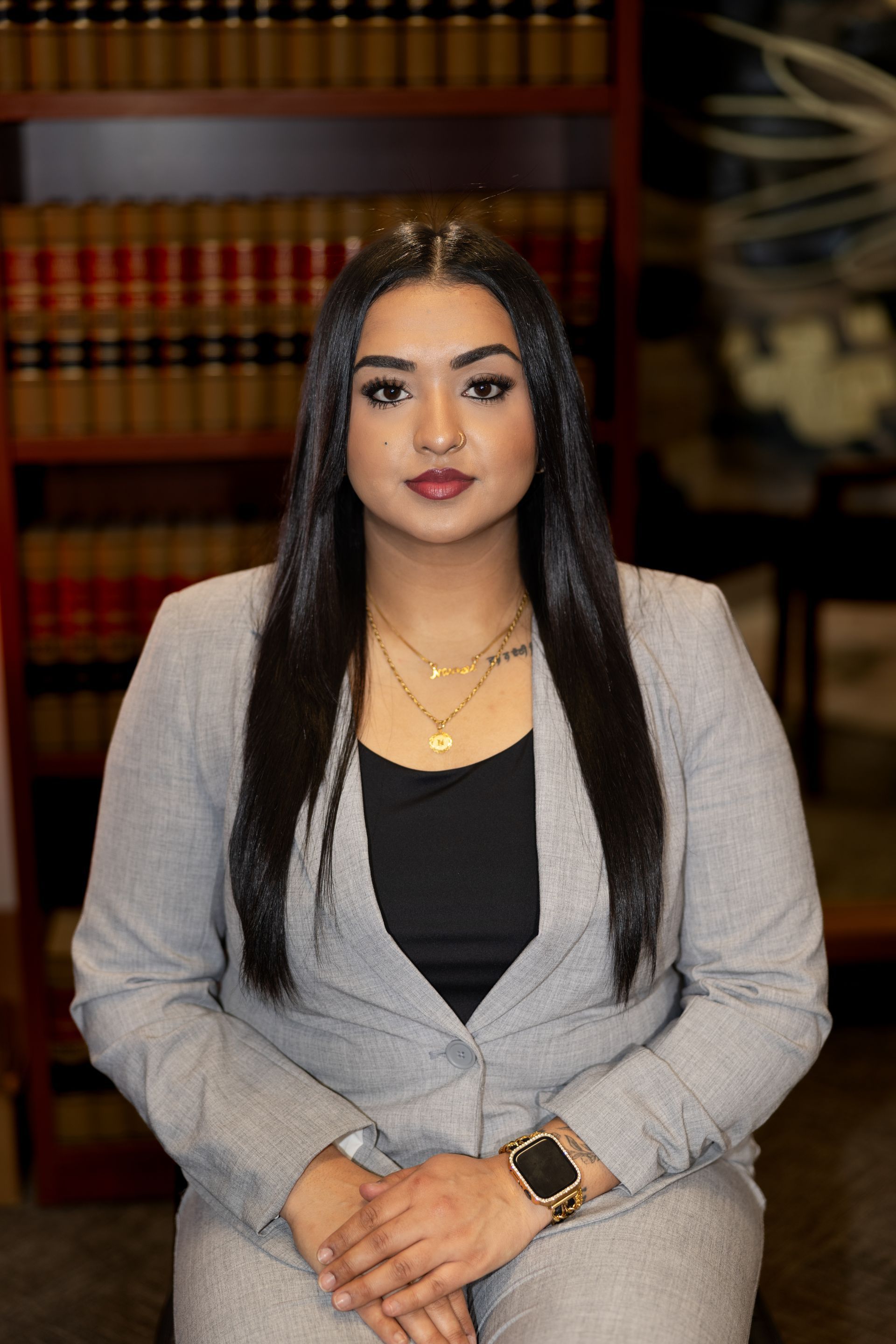 A woman in a suit is sitting in front of a bookshelf.