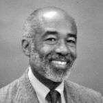 A black and white photo of a man with a beard wearing a suit and tie.