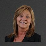 A woman in a black jacket is smiling for the camera.