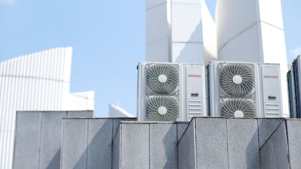 Three outdoor HVAC units atop a gray rooftop against a blue sky and white building panels