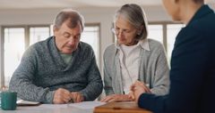 An elderly couple is sitting at a table talking to a woman.