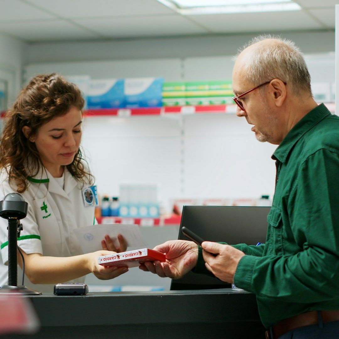 Pharmacist handing medication to a man at a pharmacy counter.