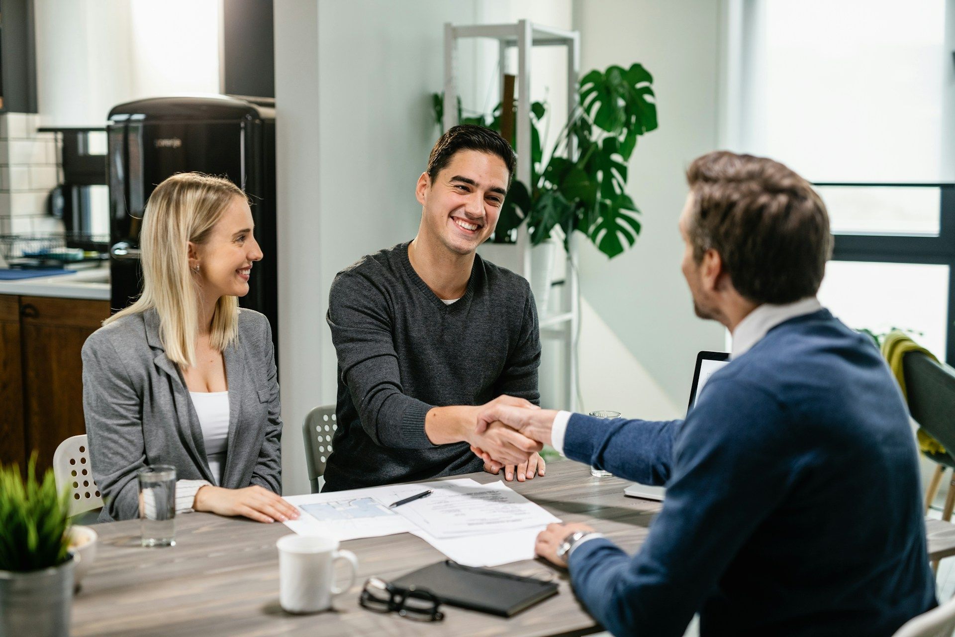 A couple and advisor shaking hands at a table, signing documents in a home office.