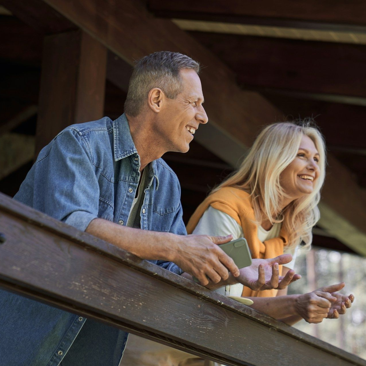 Man and woman smiling on a porch. The man wears denim, the woman wears orange.