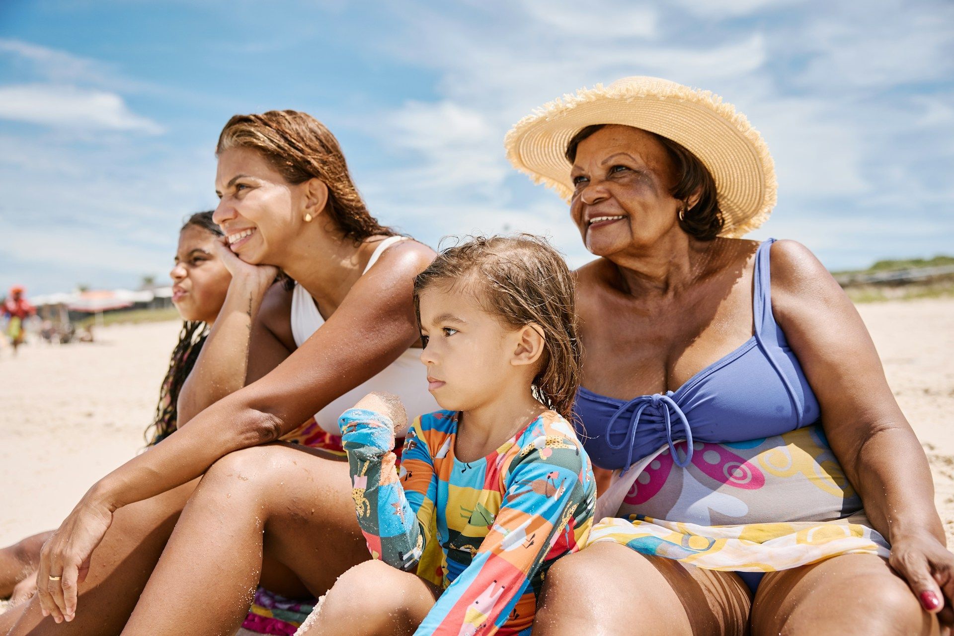 Family of four sitting on beach, smiling at the sun.