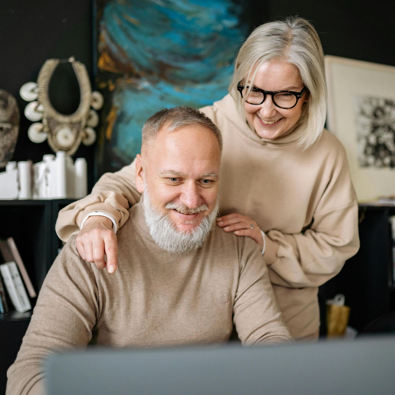 Senior couple smiling, looking at a laptop, woman pointing.