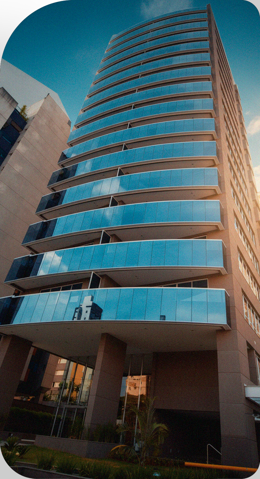 Edifício alto e moderno com muitas varandas de vidro azul sob um céu azul.