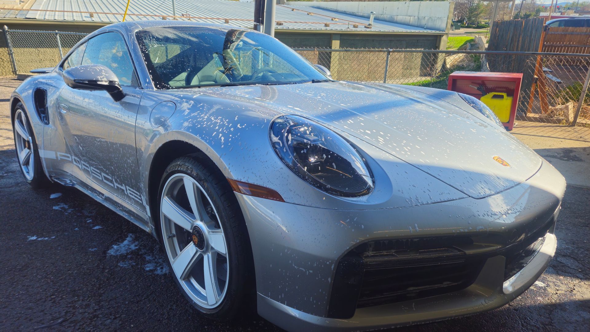 Silver Porsche 911 being washed at a car wash. The car is covered in suds.
