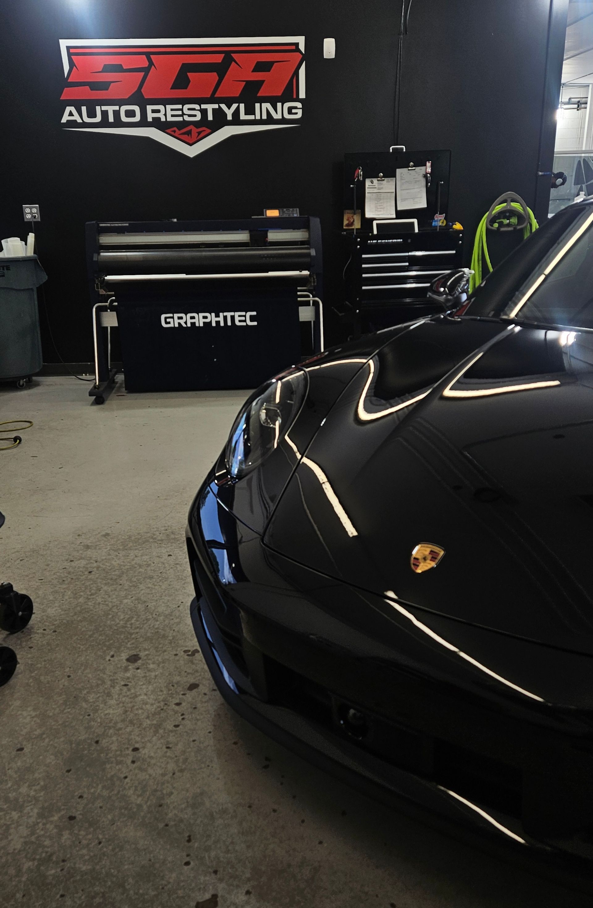 Black Porsche in a shop, logo for SGA Auto Restyling visible.