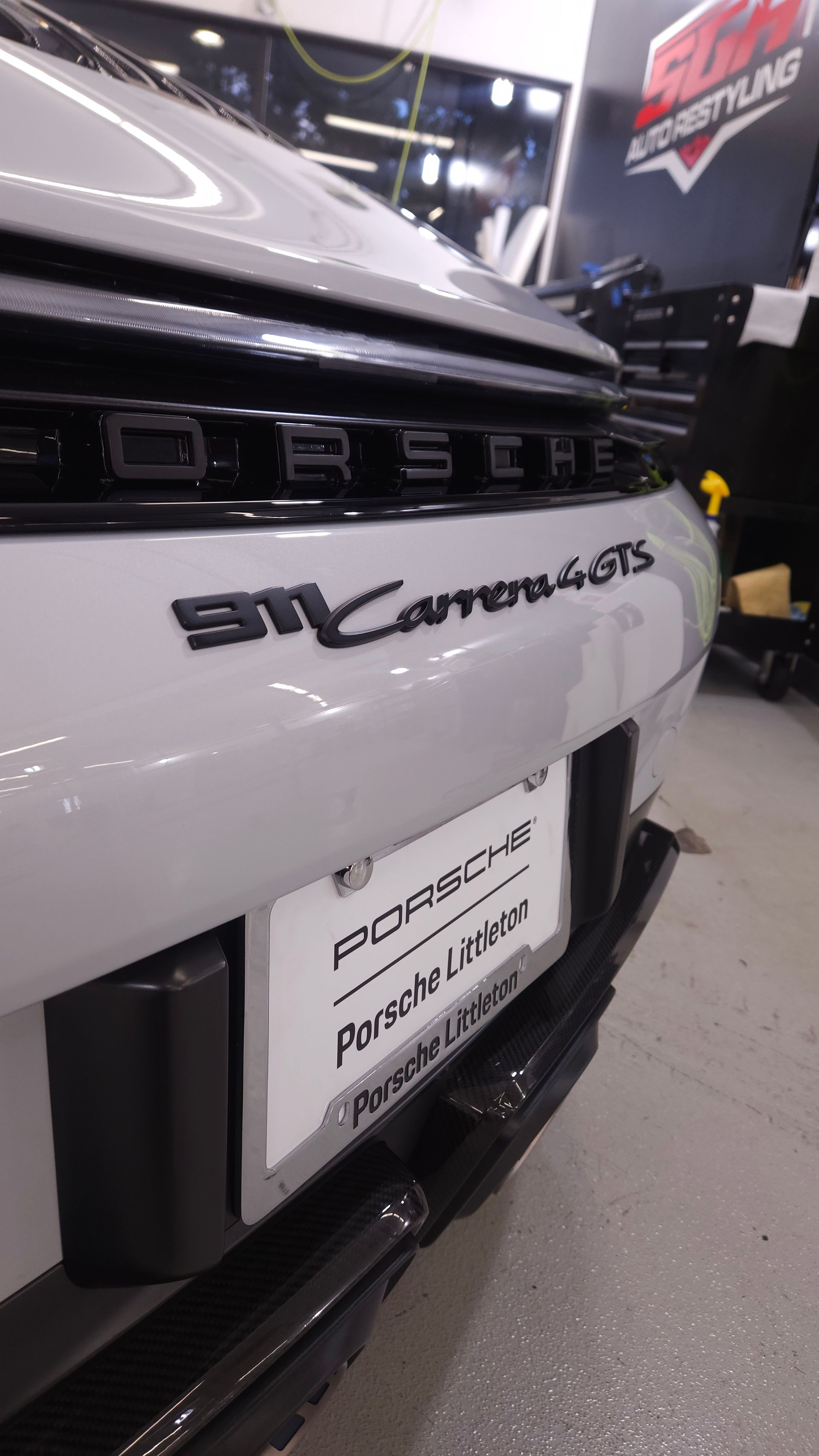 Rear view of a white Porsche 911 Carrera 4 GTS with black lettering and a license plate, in an indoor setting.