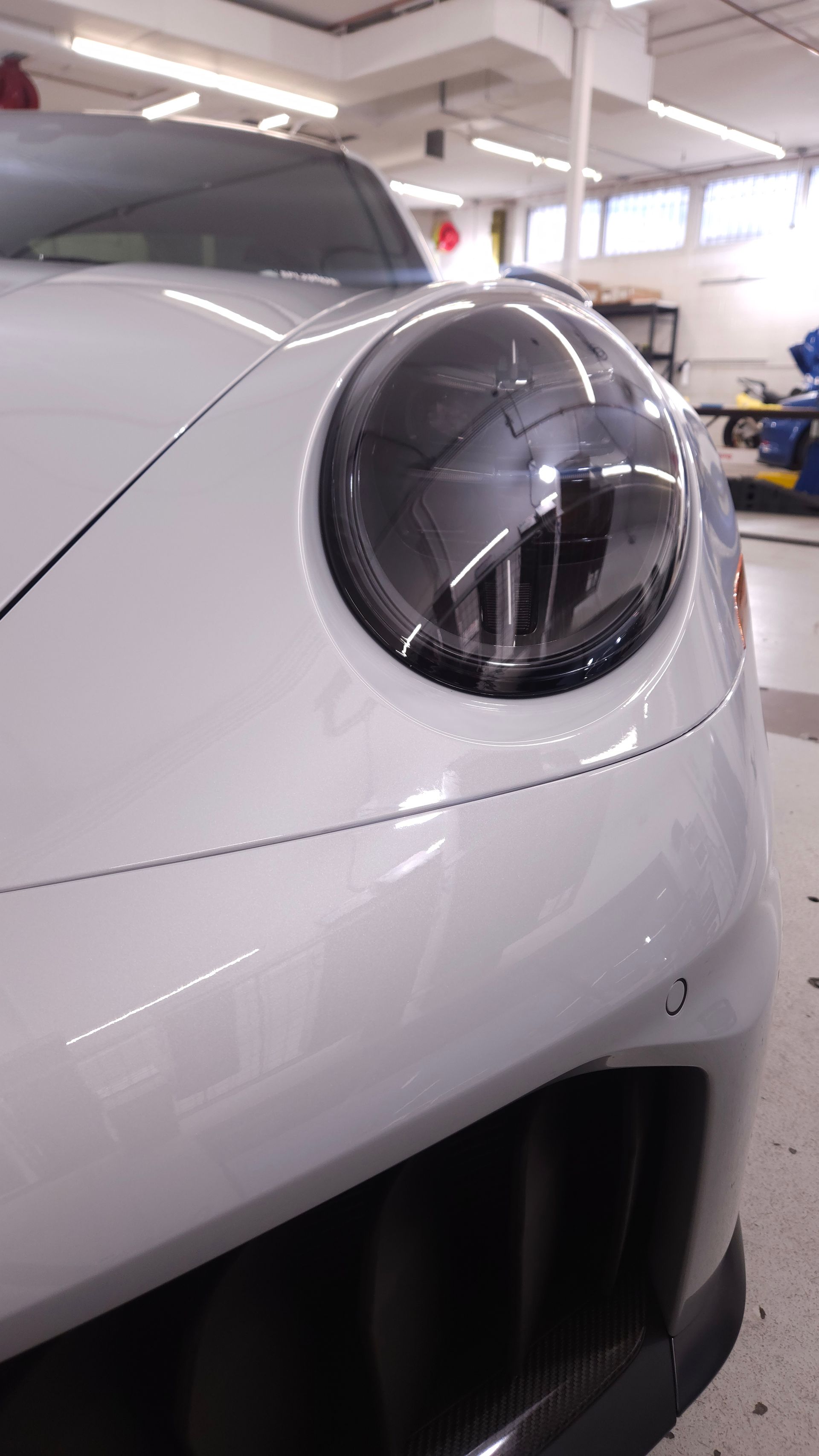 White Porsche car headlight, close-up. Blacked-out lens. Shop interior with bright lighting.