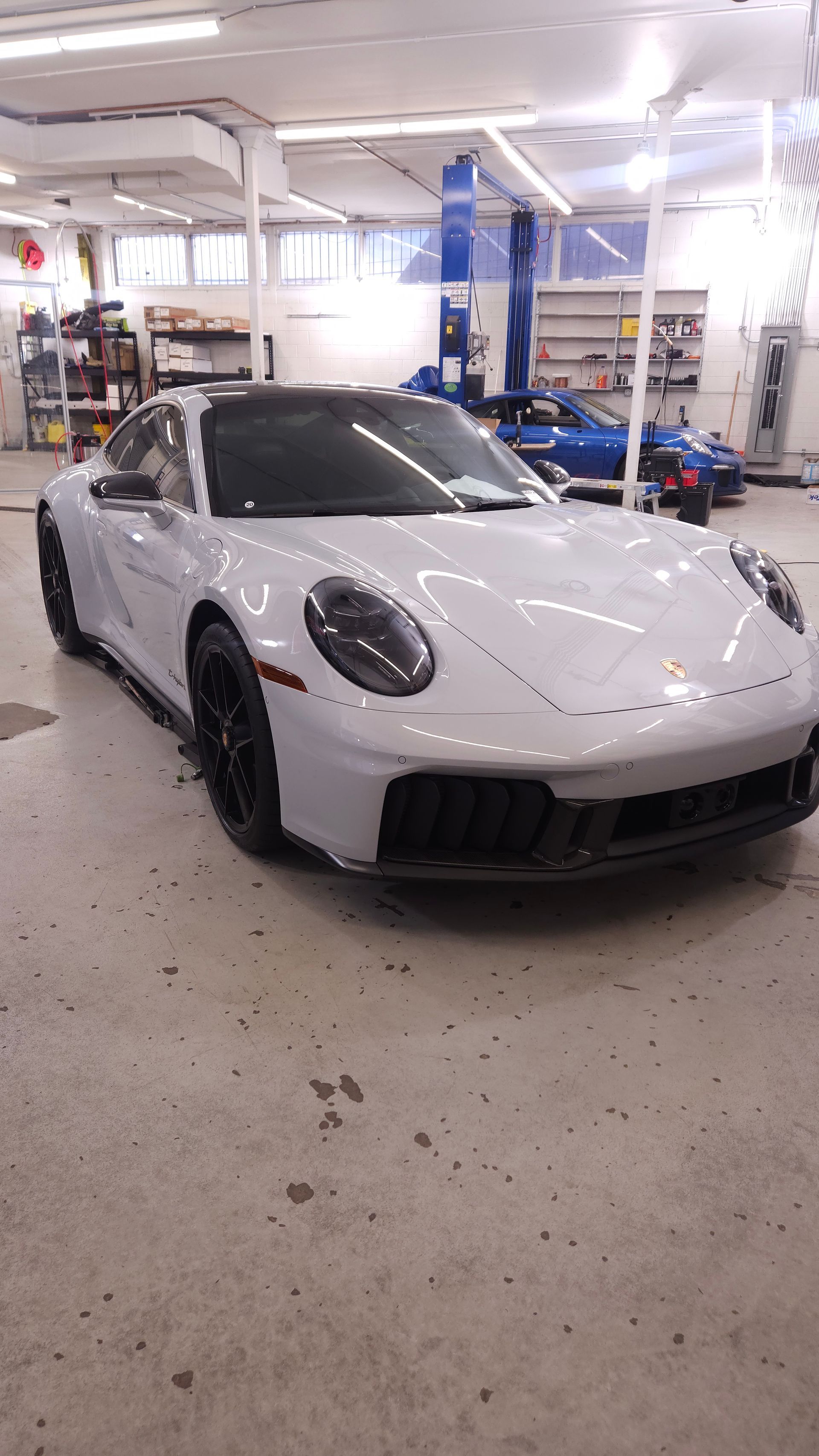 Light gray Porsche 911 sports car in a garage with a car lift in the background.