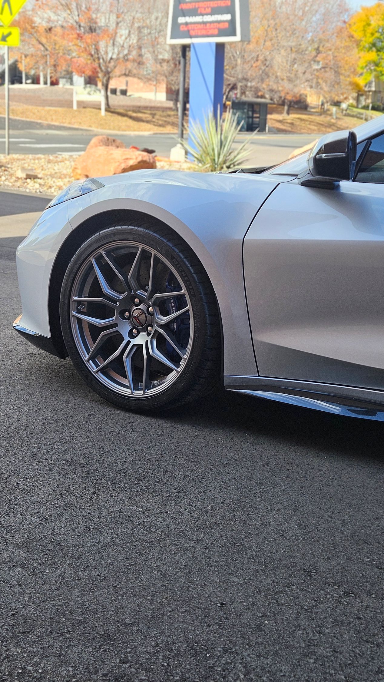 Silver sports car with black wheels parked outside a business.