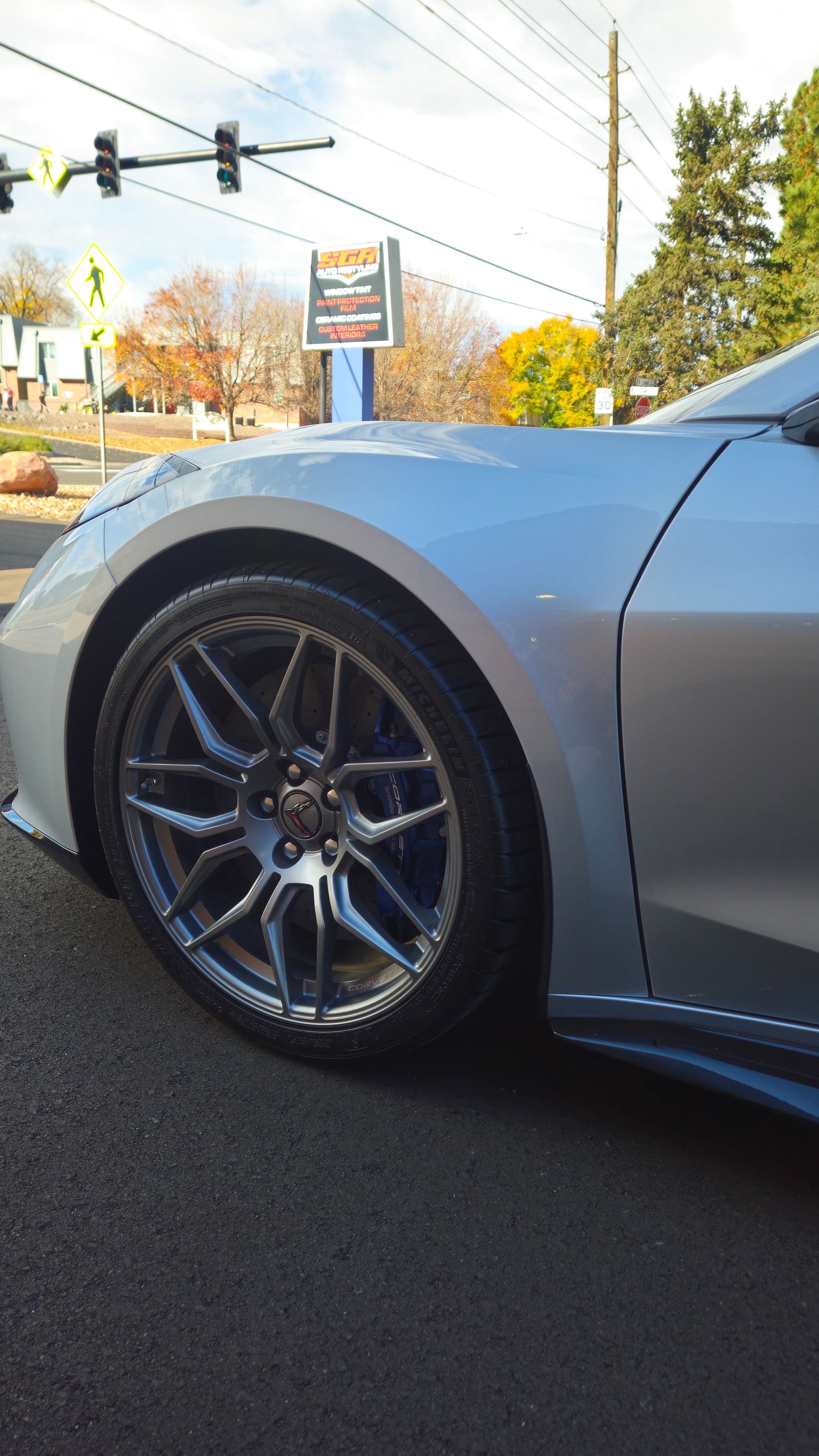 Silver car's front quarter panel and wheel. Gray rim, black tire, and asphalt road.