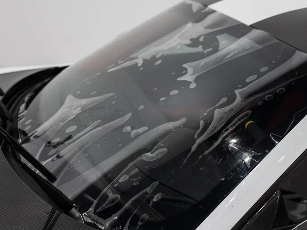 Windshield of a white and black car with protective film applied, showing bubbles and water.