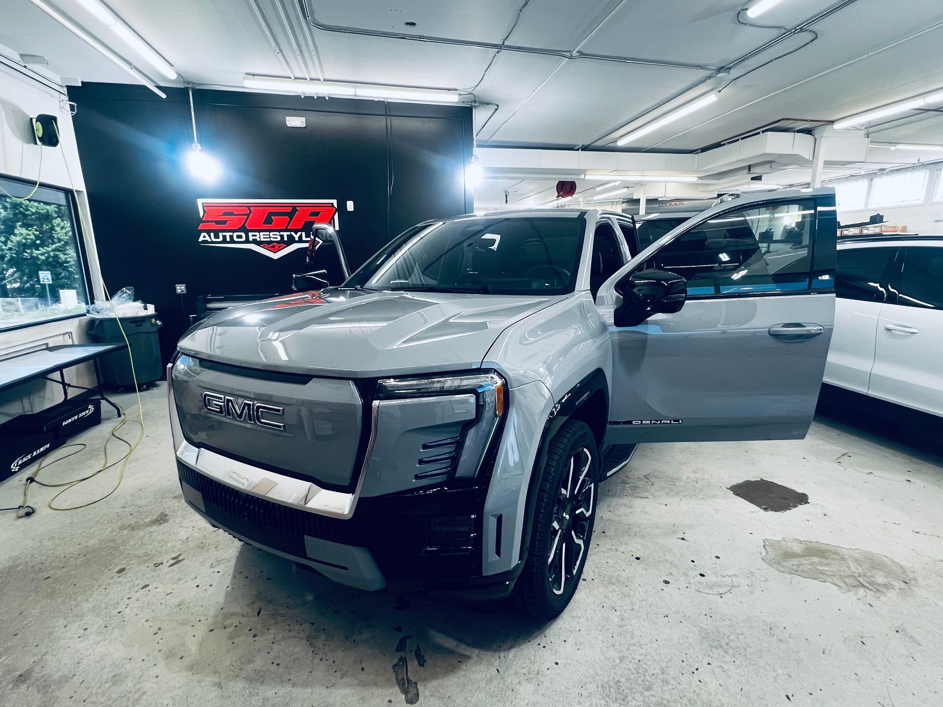 Gray GMC electric pickup truck with door open inside auto shop.