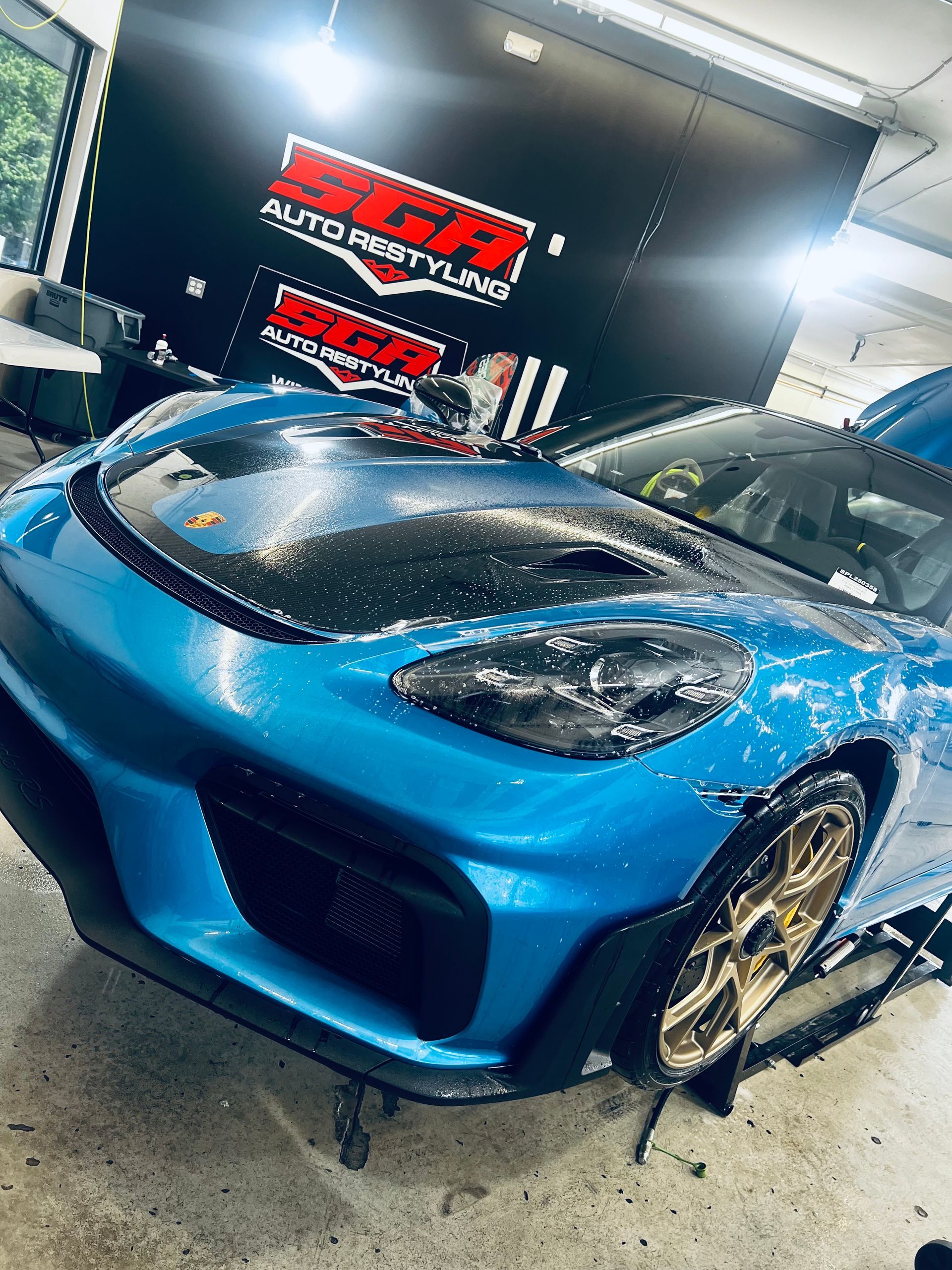 Blue sports car with a black hood being washed at a car detailing shop; gold wheels.