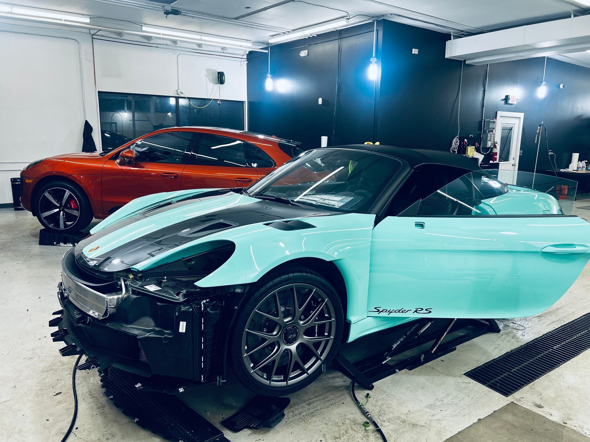 A turquoise sports car with a black stripe, and a red car in a garage.