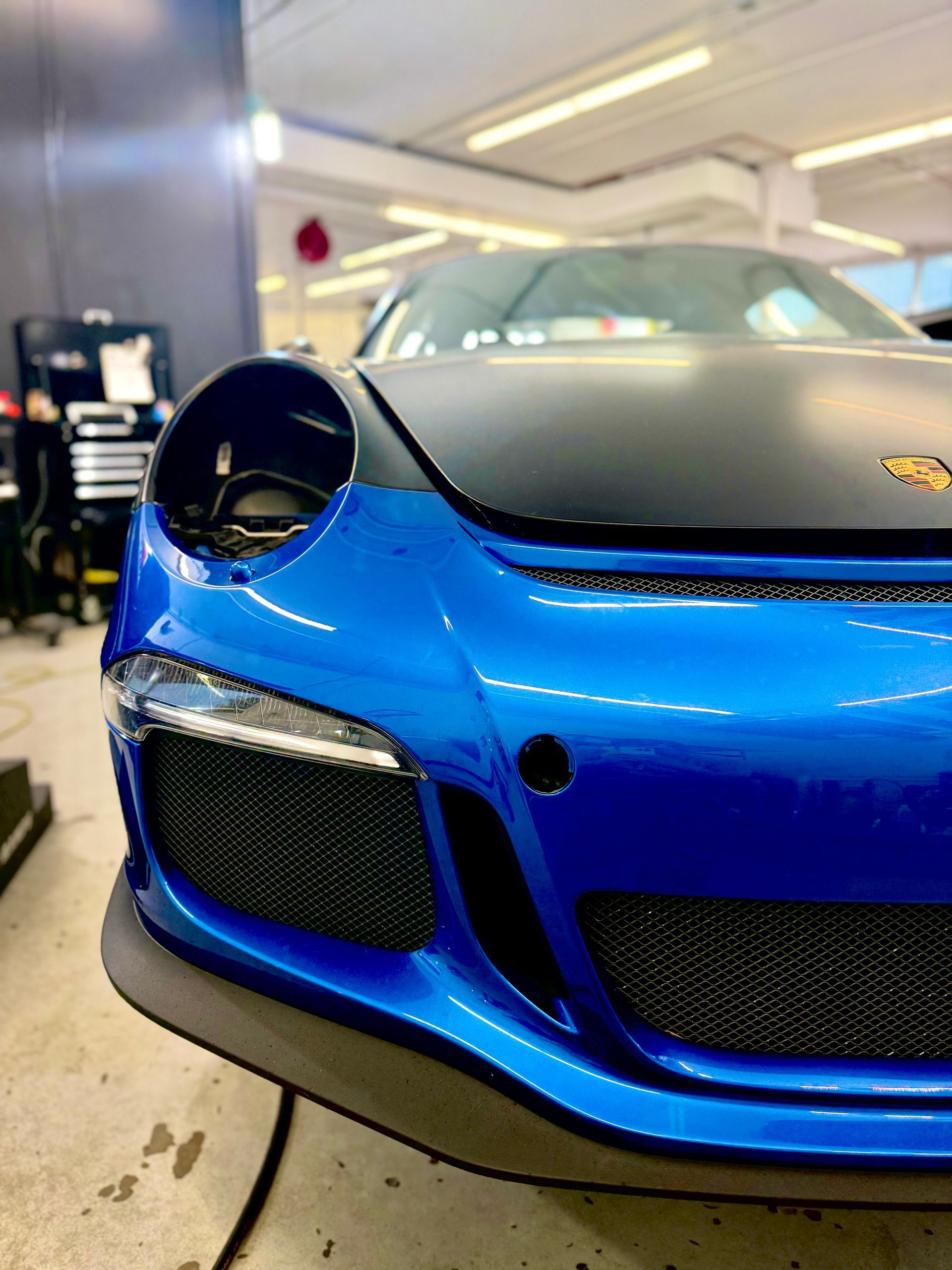 Blue and black Porsche sports car in a garage with a damaged front, viewed from a close angle.