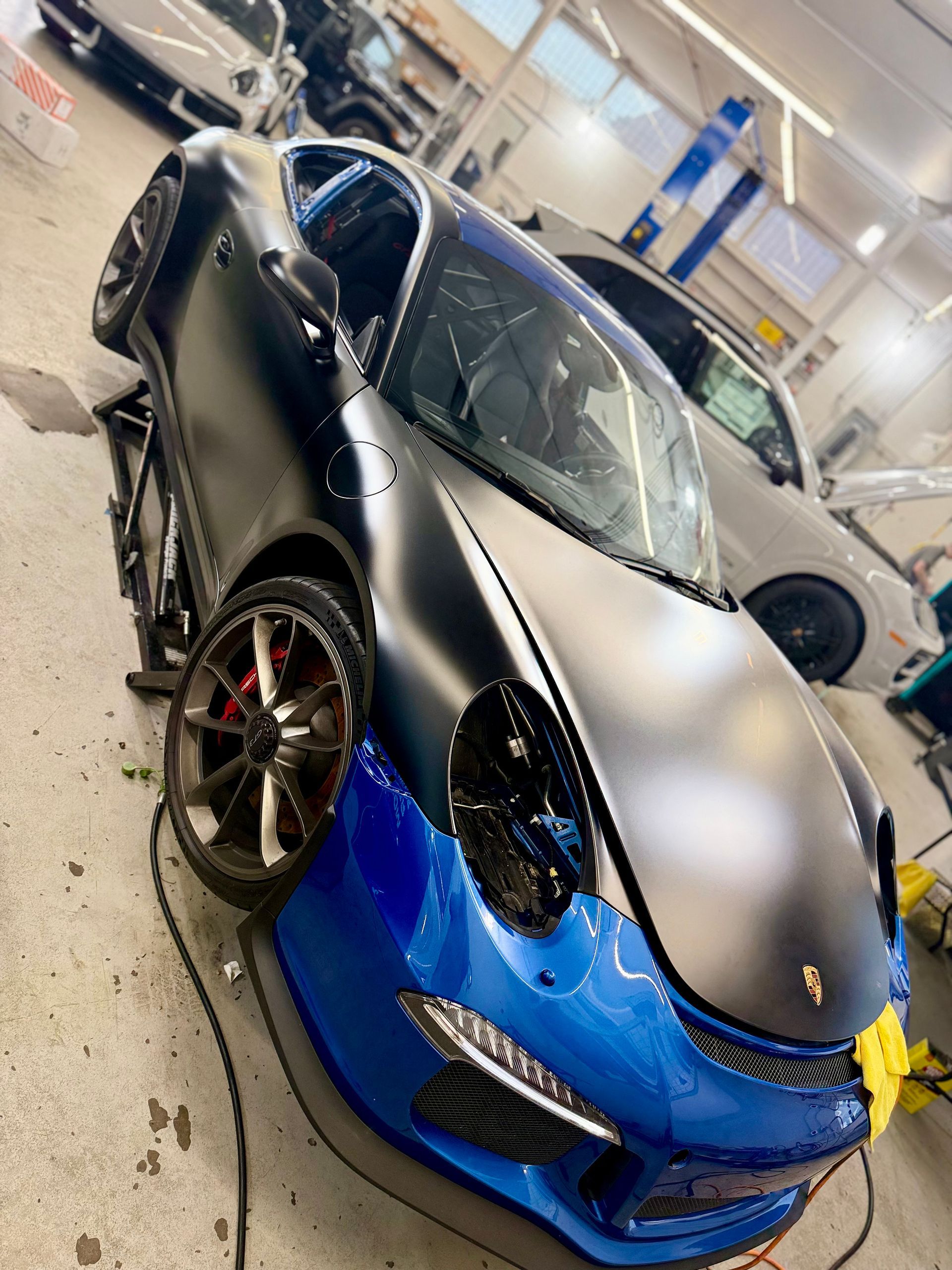 Porsche sports car with matte black and blue wrap in a garage.
