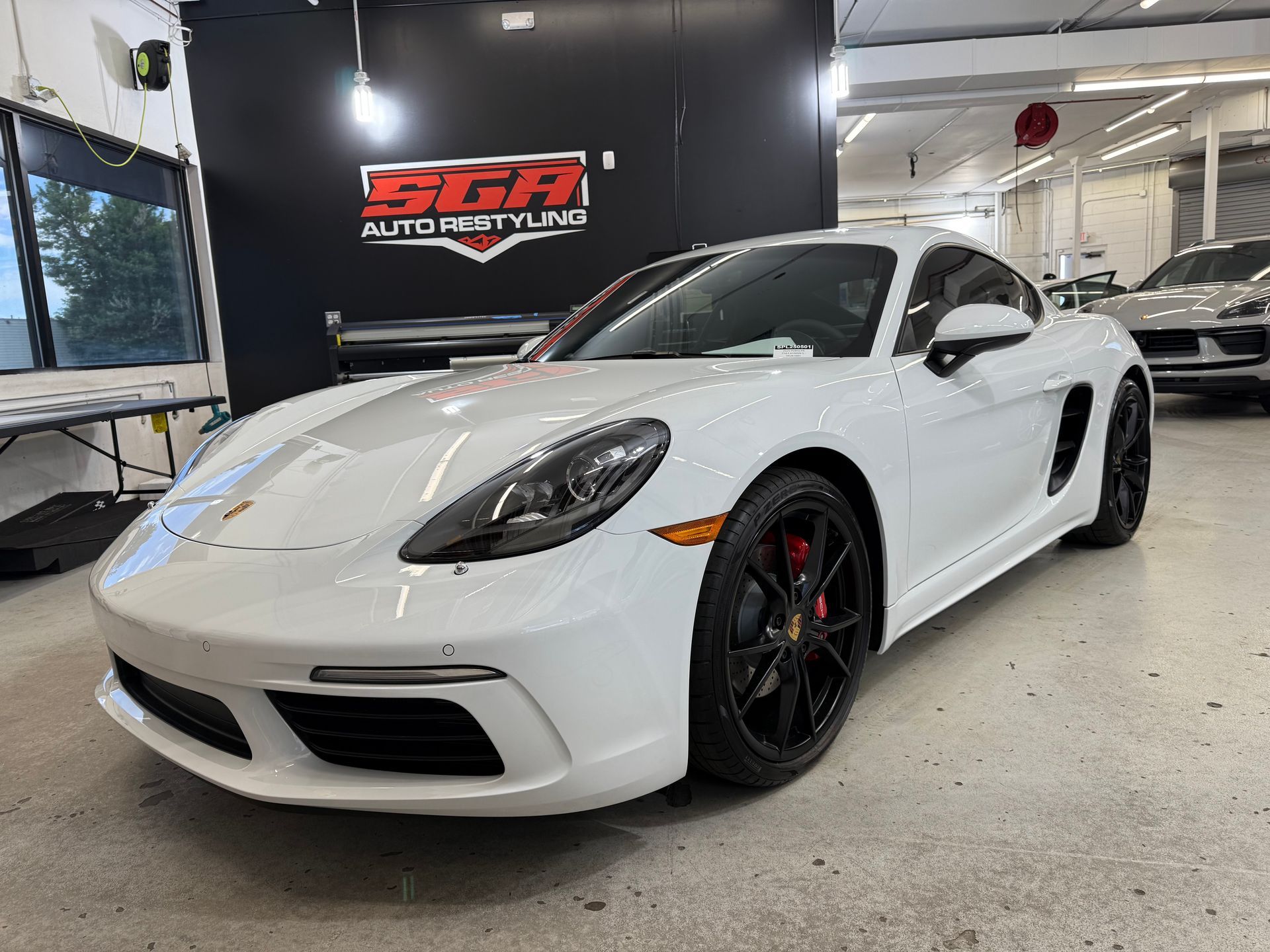 White Porsche Cayman sports car in a shop with black wheels and red brake calipers.