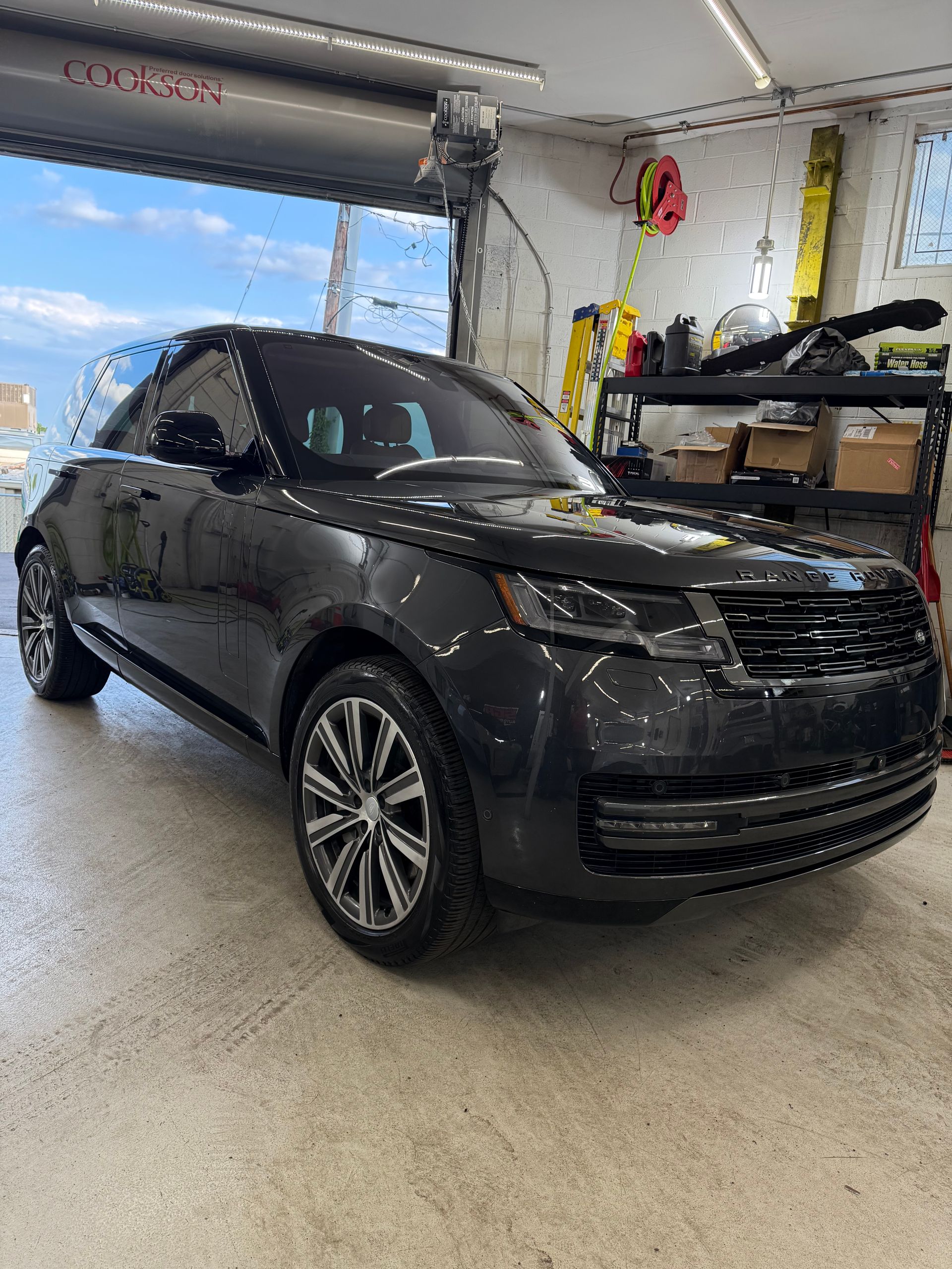 Black Range Rover SUV parked in a garage with tools and open door to sky.