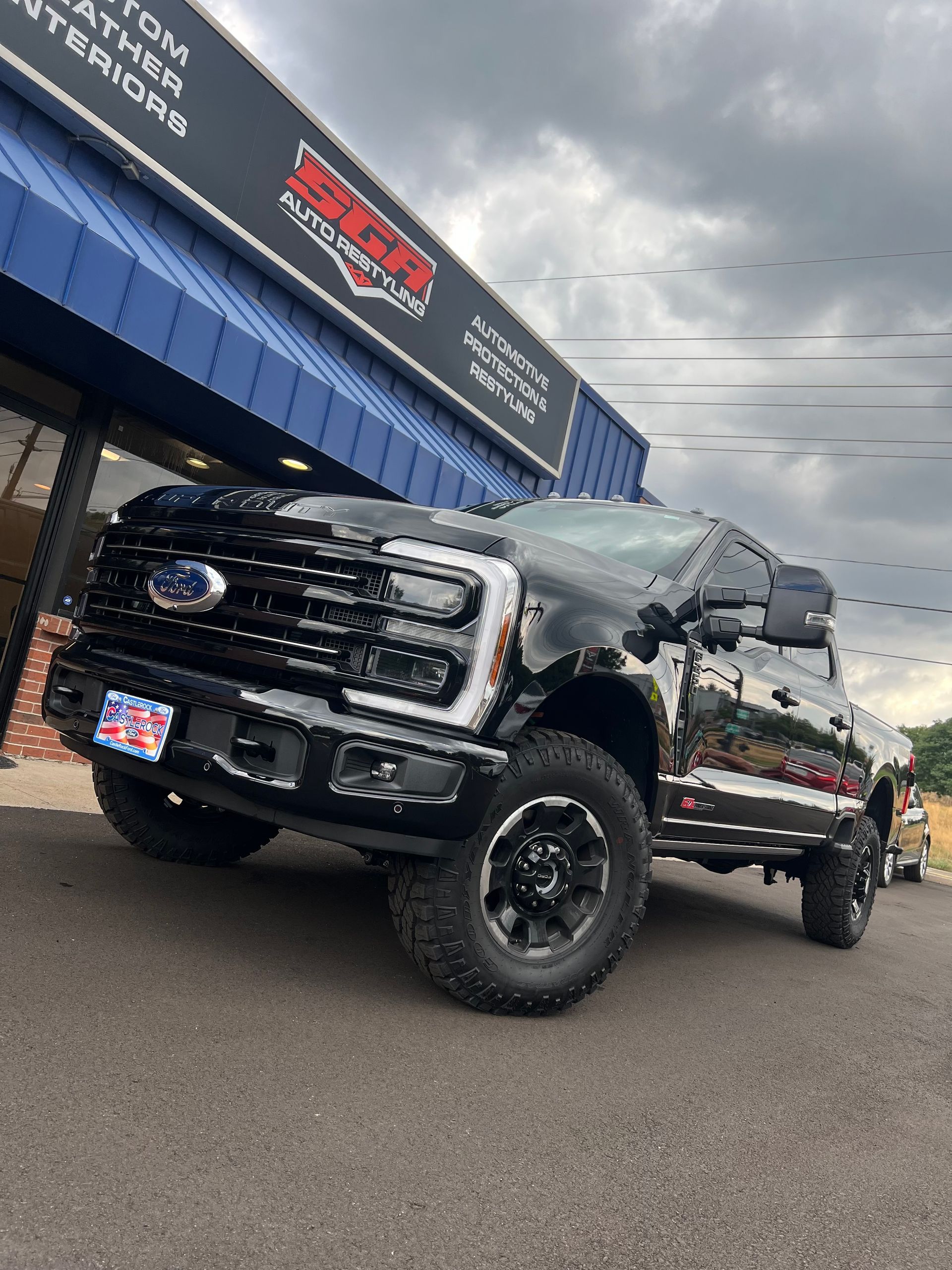 Black Ford pickup truck parked outside a business with a blue awning; cloudy sky.